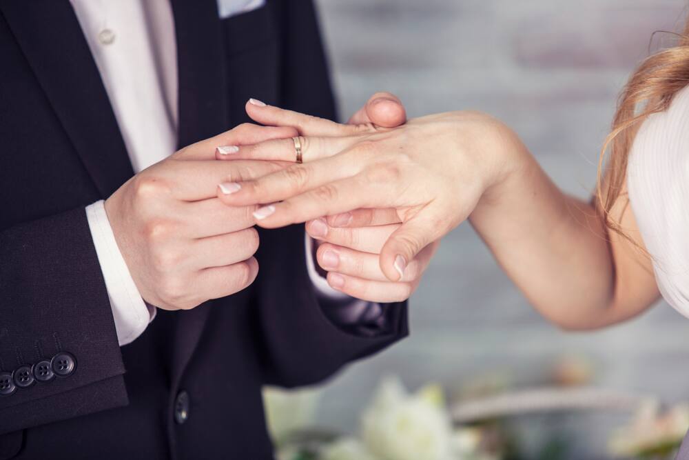 A groom putting a ring on the ring finger of the bride on the day of the wedding ceremony.