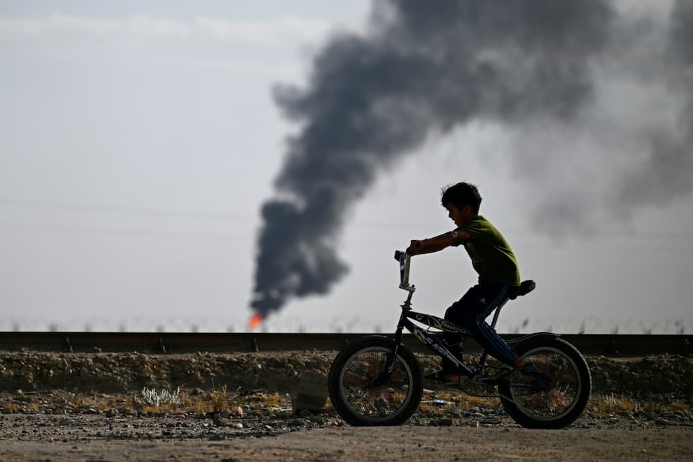 Children play football or ride their bicycles, seemingly unaware of the danger of the gas flaring around them
