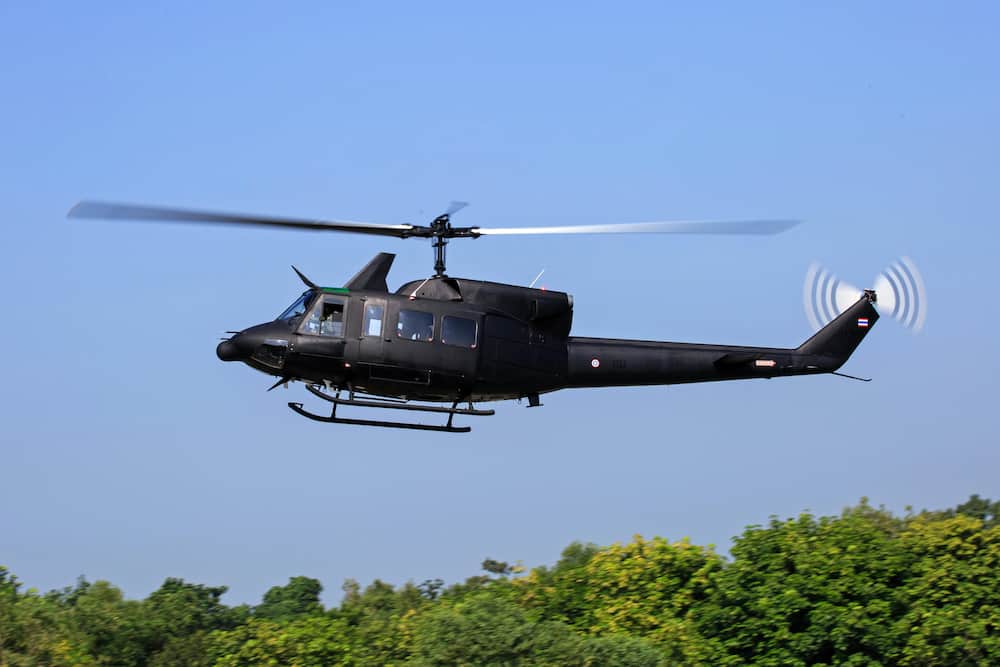 A black helicopter flying over green trees