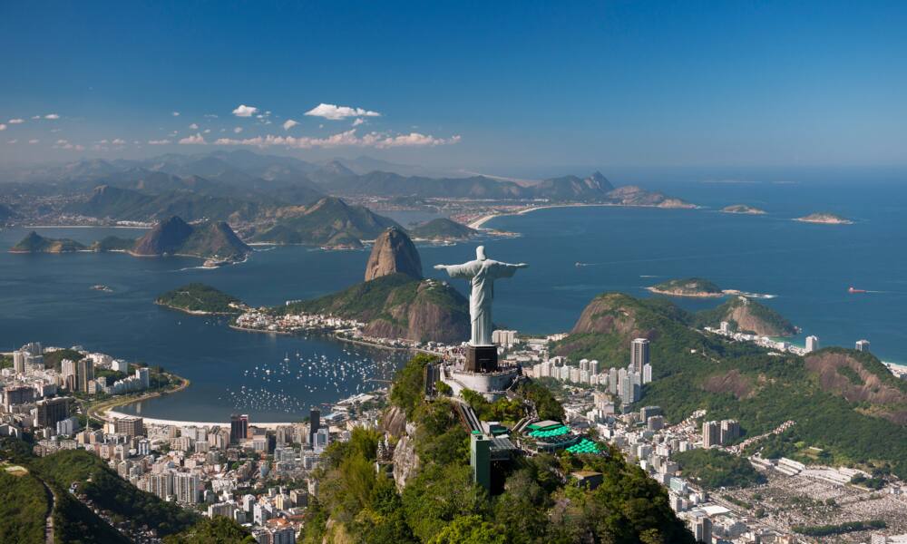 Aerial view of the 'Christ The Redeemer' statue, with Sugarloaf Mountain and Botafogo Beach in the background.