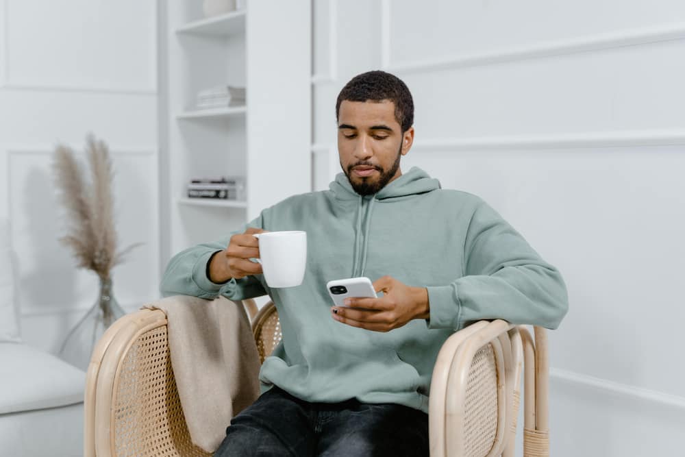 A man using a smartphone while enjoying a cup of tea