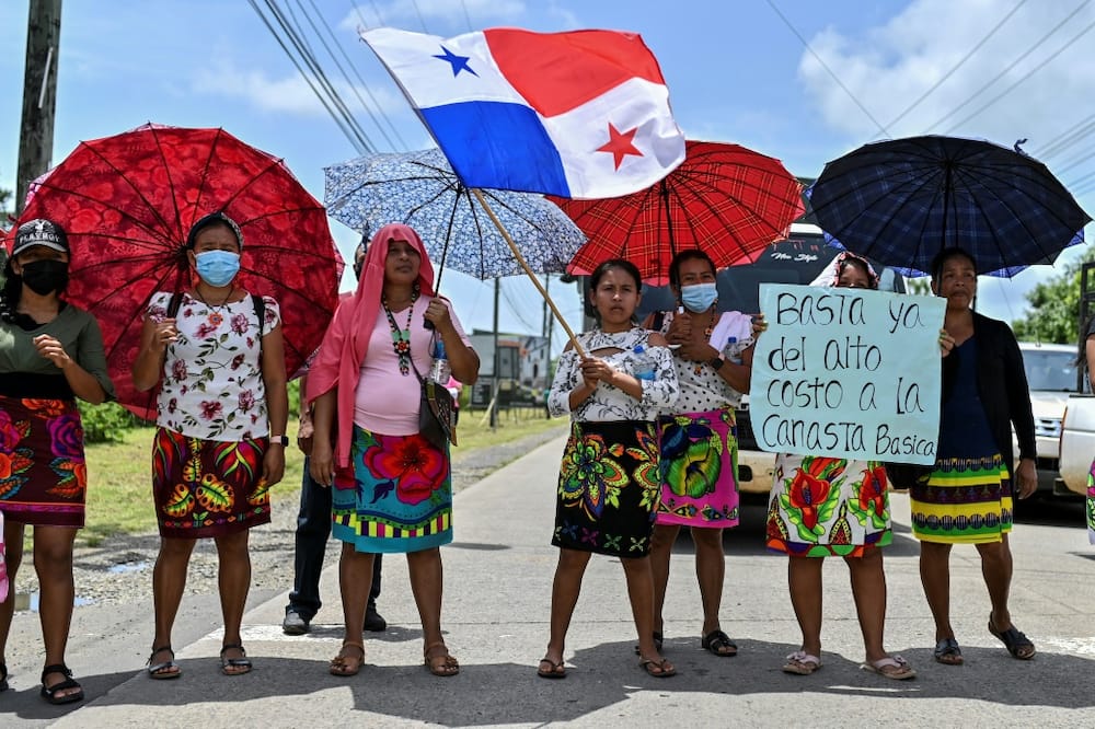 Embera indigenous women with umbrellas and a Panamanian flag block the Pan-American highway during a protest against fuel prices on July 20, 2022