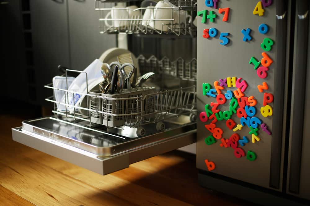 Dishwashing machine with open drawer next to refrigerator covered in childrens' fridge magnets