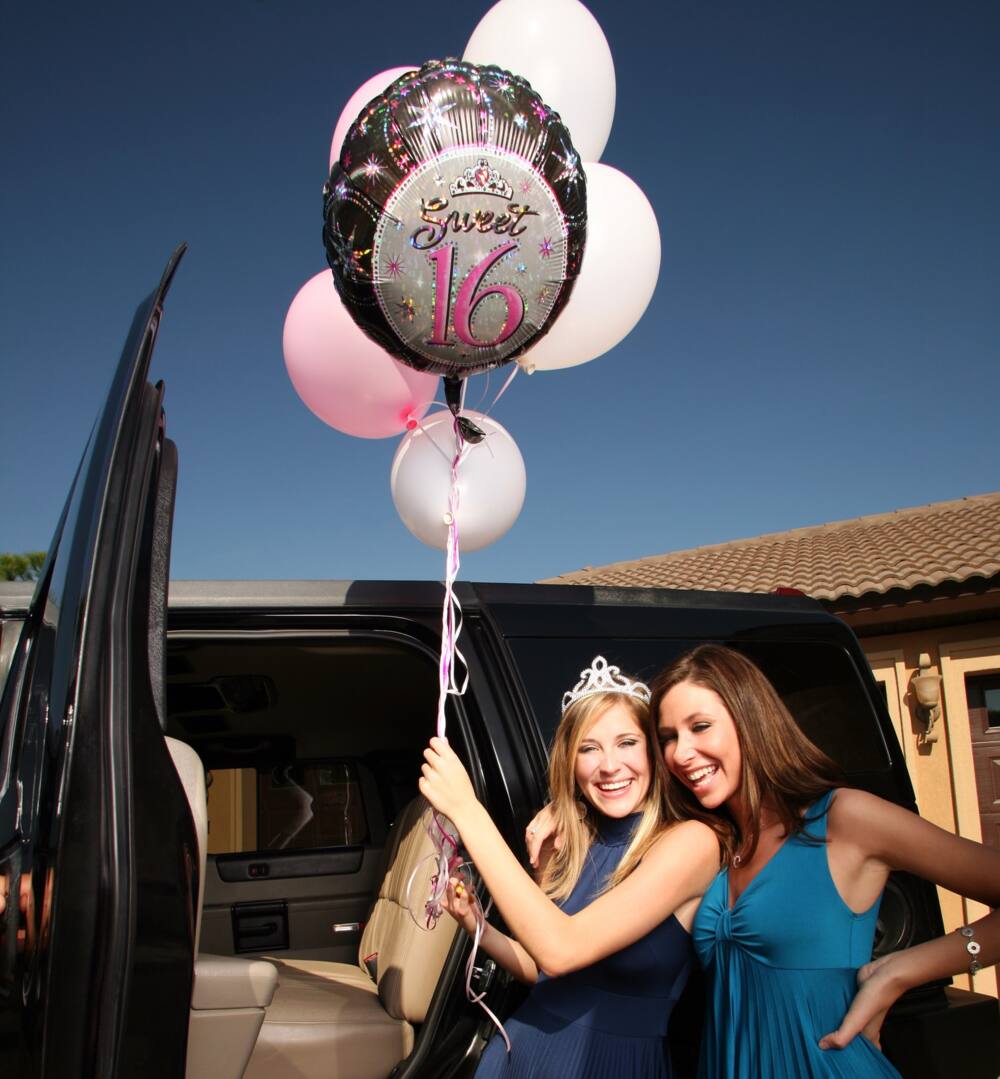 two teenage girls with balloons beside a car