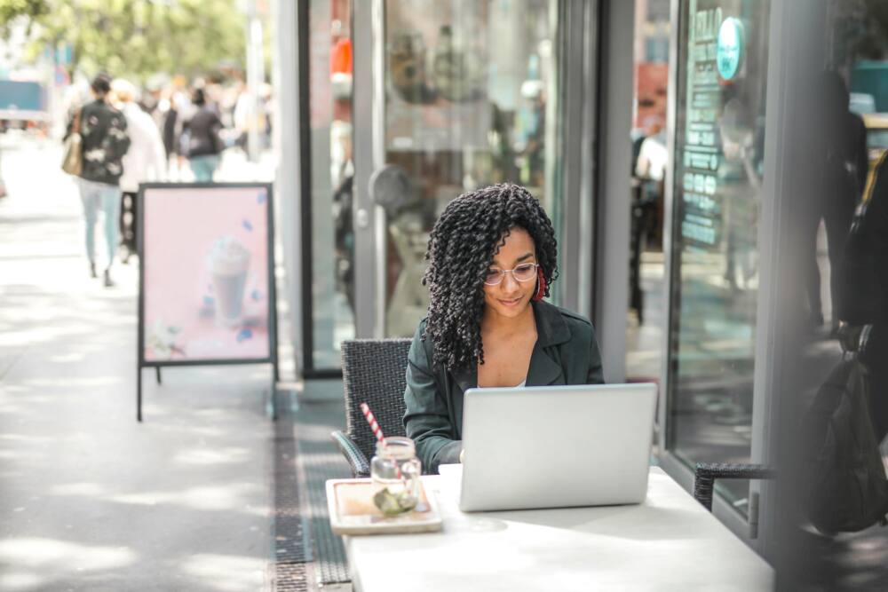 A woman in glasses using a laptop outside a coffee shop