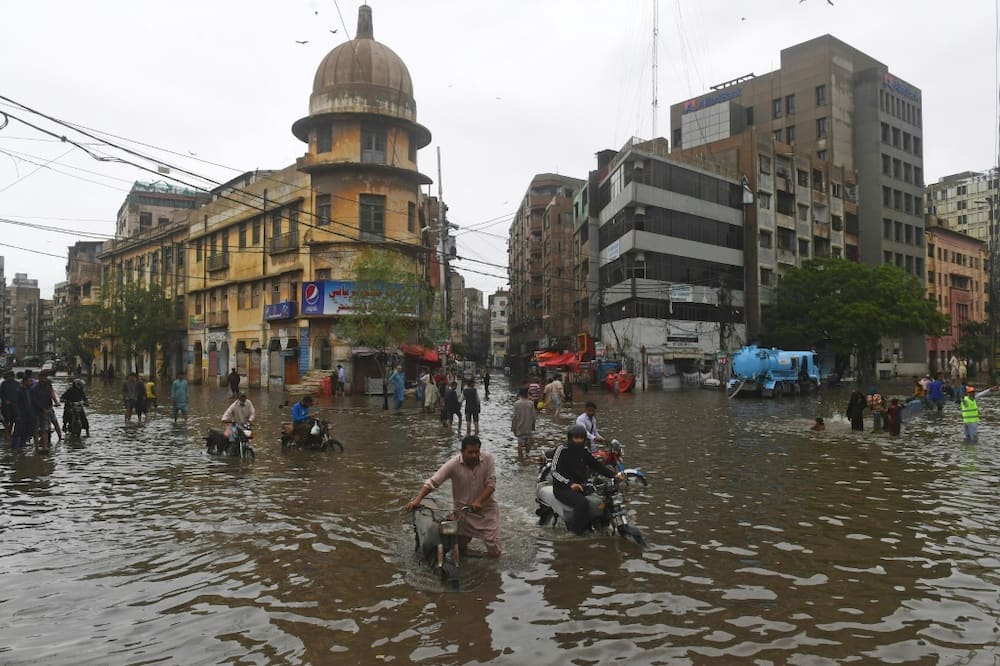 Motorcyclists push their vehicles through a flooded street in Pakistan's port city of Karachi
