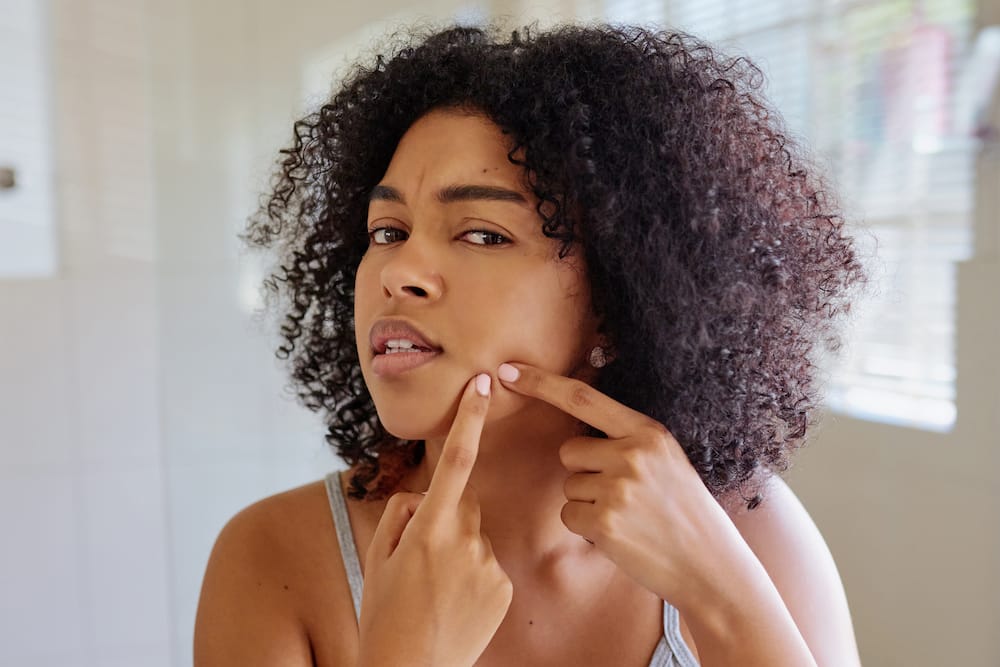 A woman squeezing a pimple on her cheek