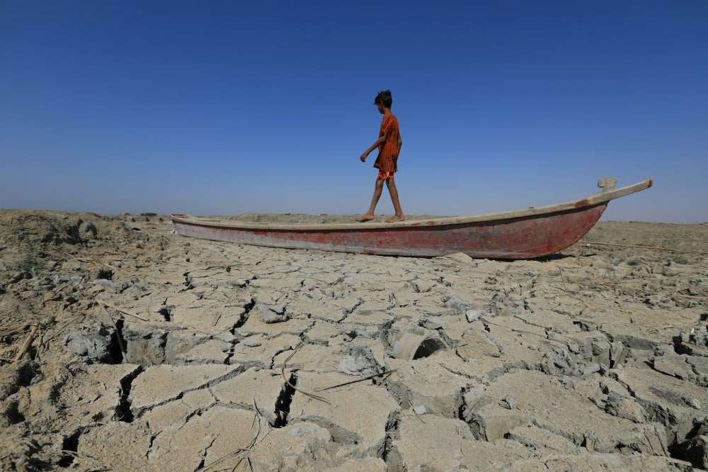 A boy walks on a boat on the dried-up bed of a section of Iraq's receding southern marshes of Chibayish in Dhi Qar province amid a drought seen as worsened by climate change