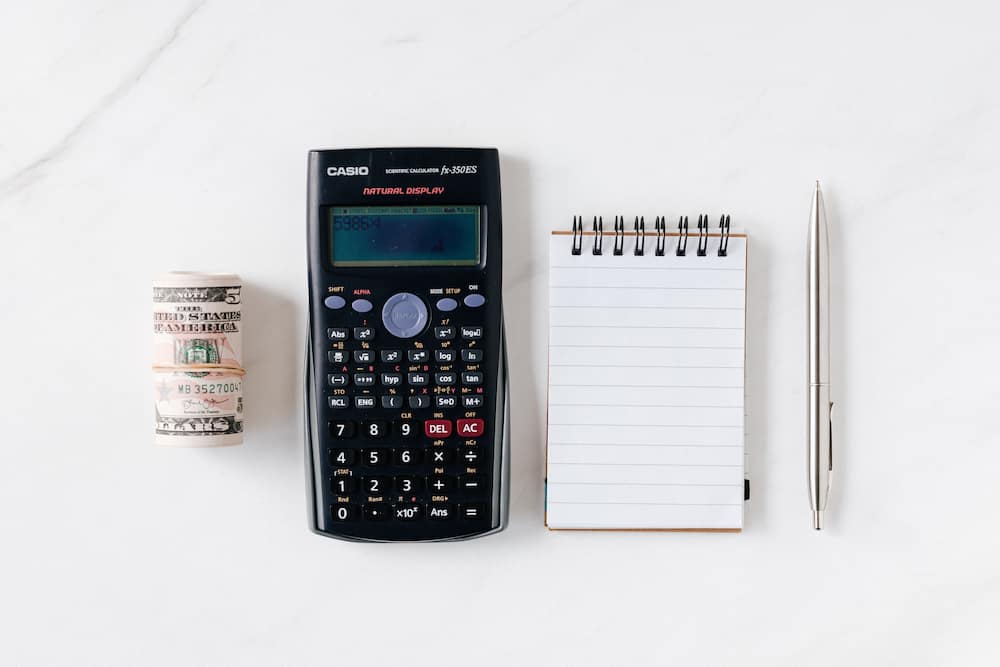 A bundle of notes, calculator, notebook and pen on a white surface