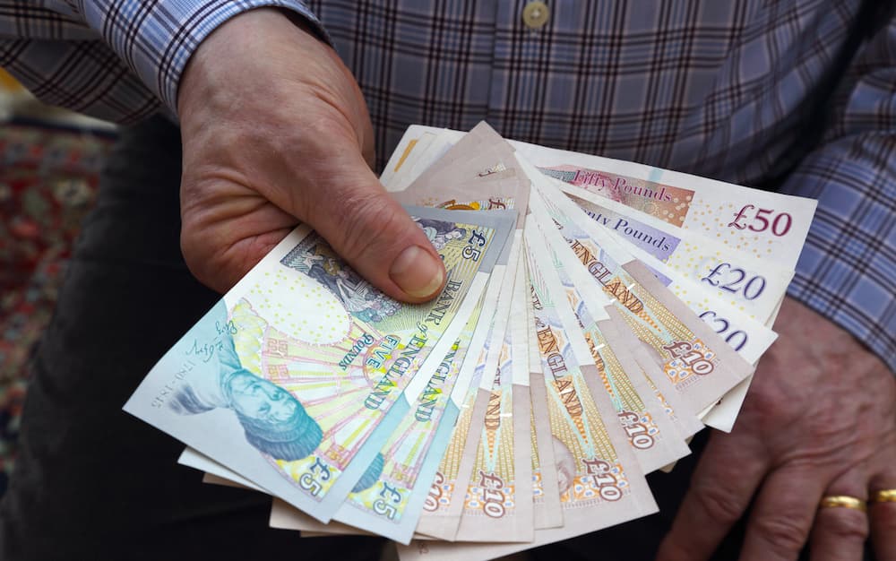 A senior male holding British banknotes in his right hand