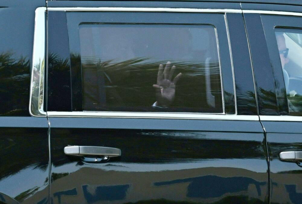 Former president Donald Trump waves as he rides in the back of an SUV to the airport in Palm Beach