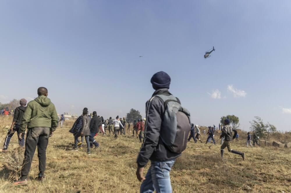 Residents run away from a police helicopter during a protest against illegal mining and rising crime in Kagiso
