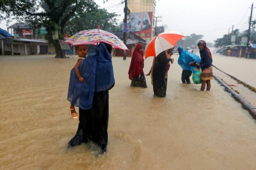 People wade along a flooded road following heavy monsoon rains in Sylhet, Bangladesh