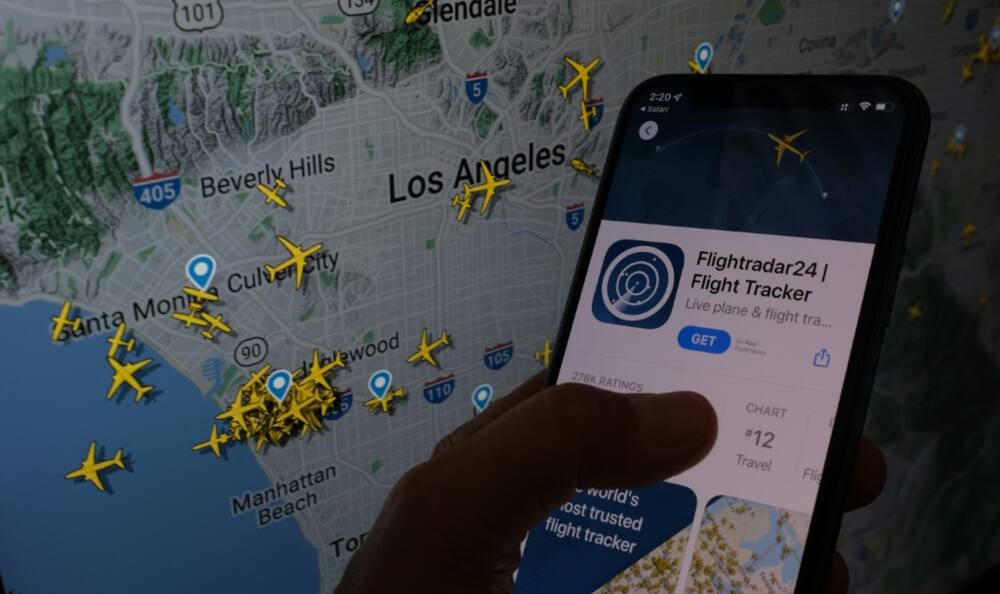 The Flightradar24 app is seen on a smartphone in front of a screen showing the live position of planes tracked by the app in the area of Los Angeles on August 5, 2022