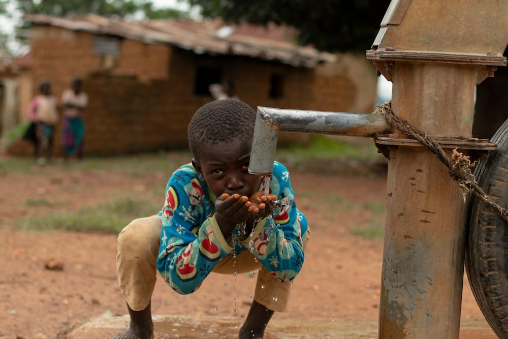 A little boy drinking water from a borehole fitted with a pump