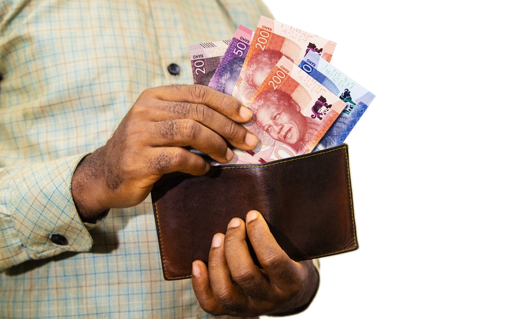 A black person holding a brown wallet with South African Rand notes