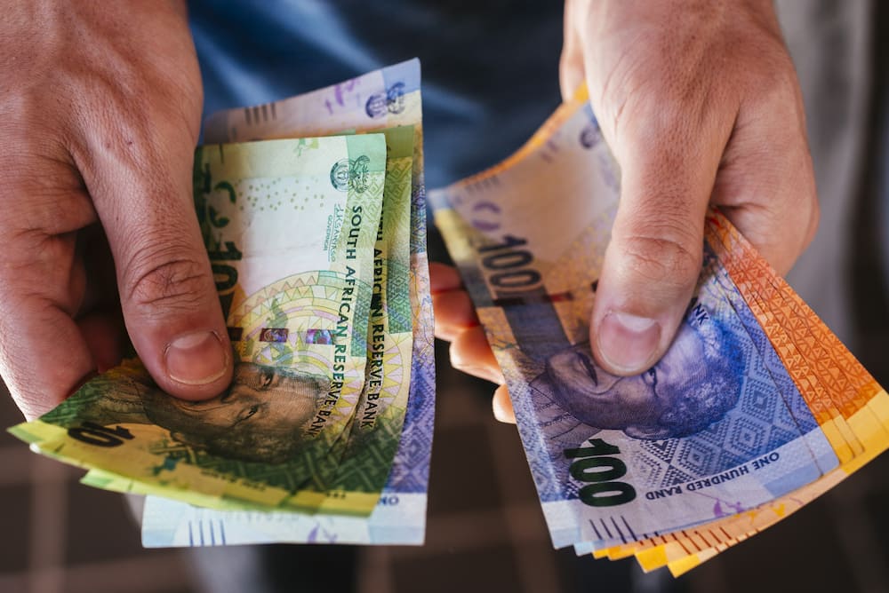 A person holding a collection of mixed denomination South African rand banknotes in Johannesburg