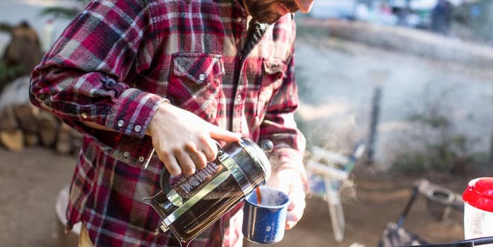 Man wearing a flannel shirt preparing coffee while camping