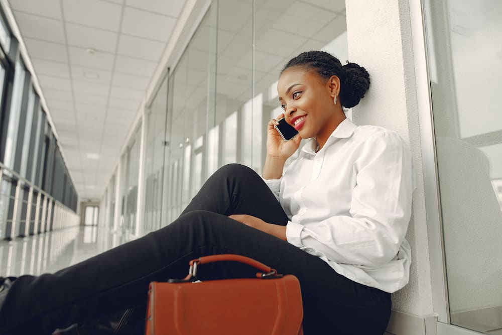 A woman in a white shirt and black pants making a phone call