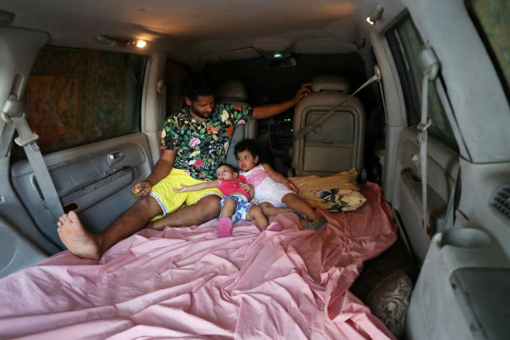 Mahmud Aguil sits with his children in the back of his air-conditioned van, his new bedroom amid power cuts and blistering summer heat