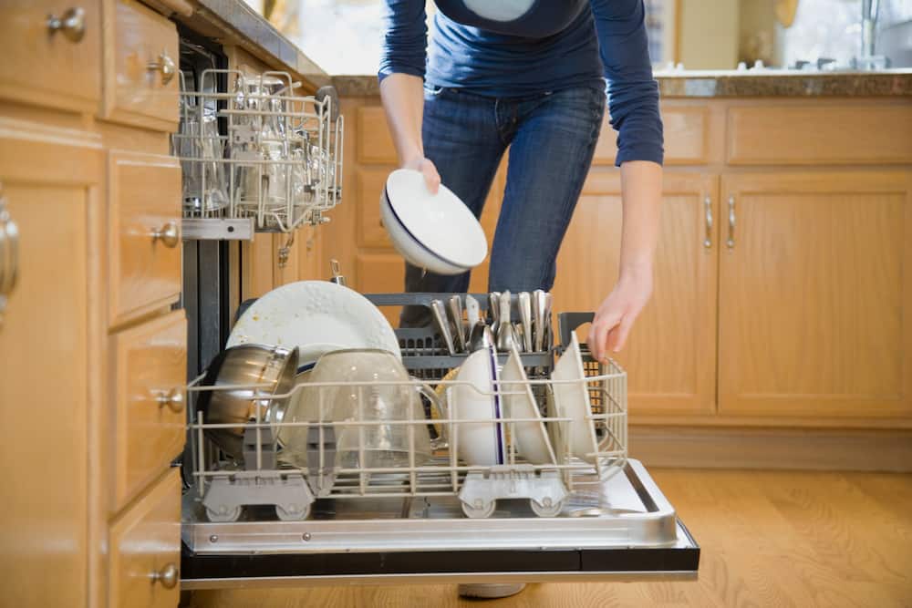 Teenage girl putting dishes in dishwasher, low section