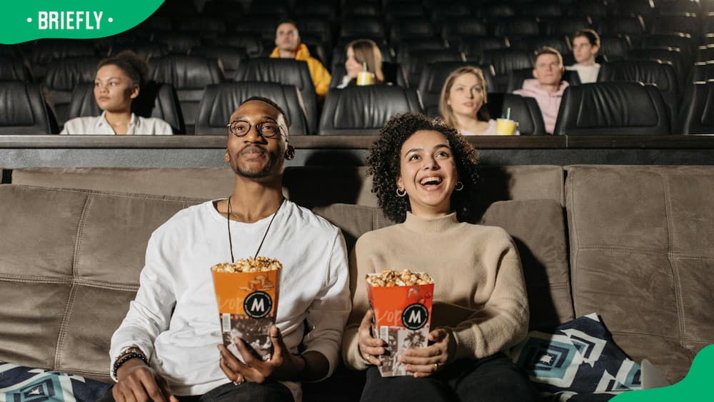 A couple holding popcorns while watching a movie.