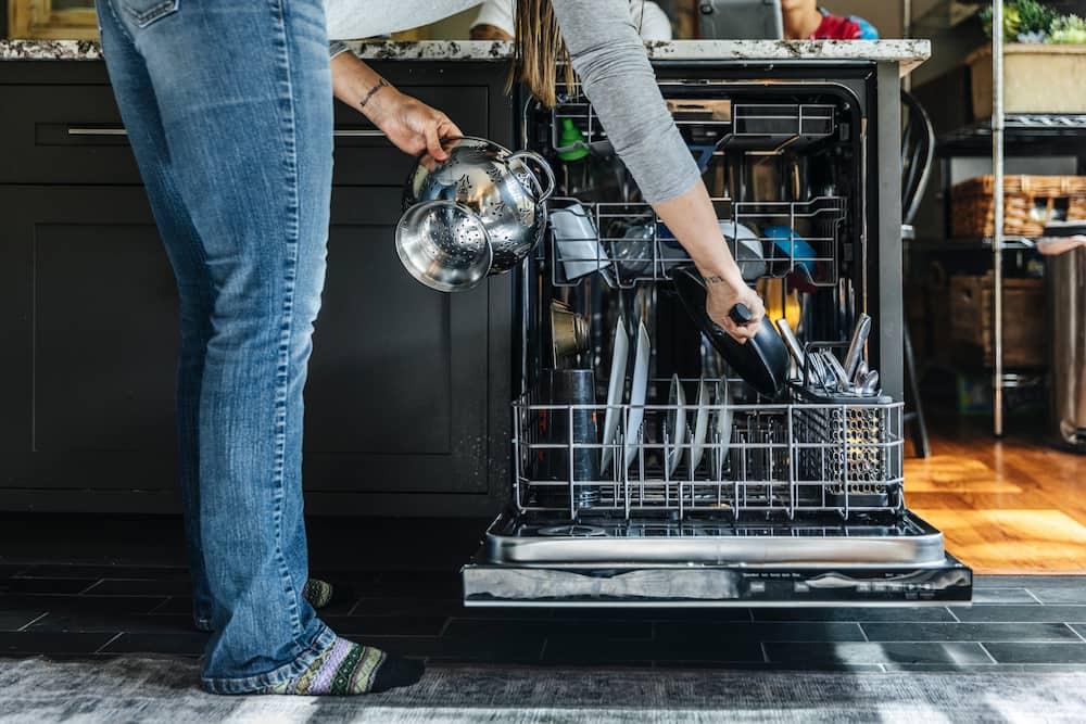 Woman arranging utensils in dishwasher at home