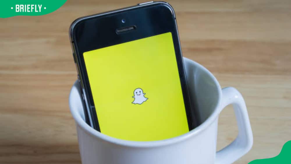 Apple iPhone5s in a mug showing its screen with Snapchat logo
