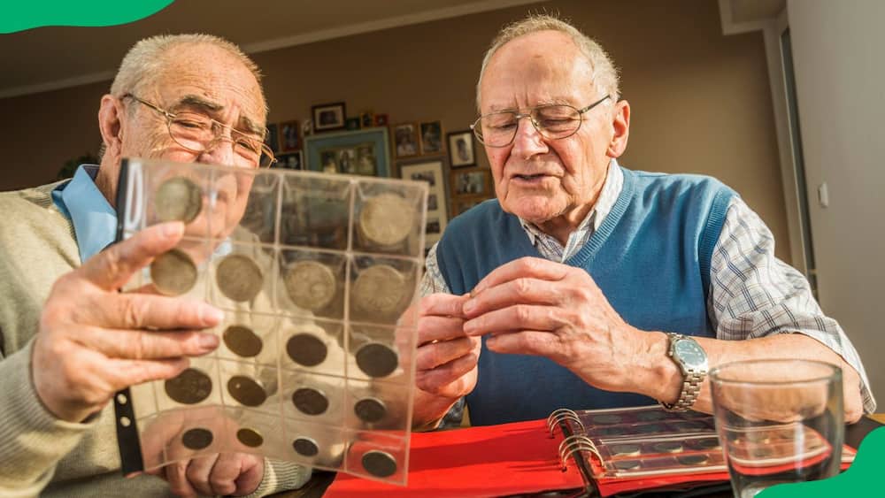 Two elderly men inspecting old South African coins